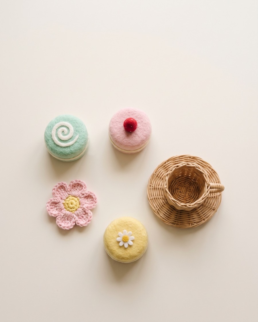 Handmade play food: needle-felted cakes, a crochet flower and a small woven cup on a plain cream surface